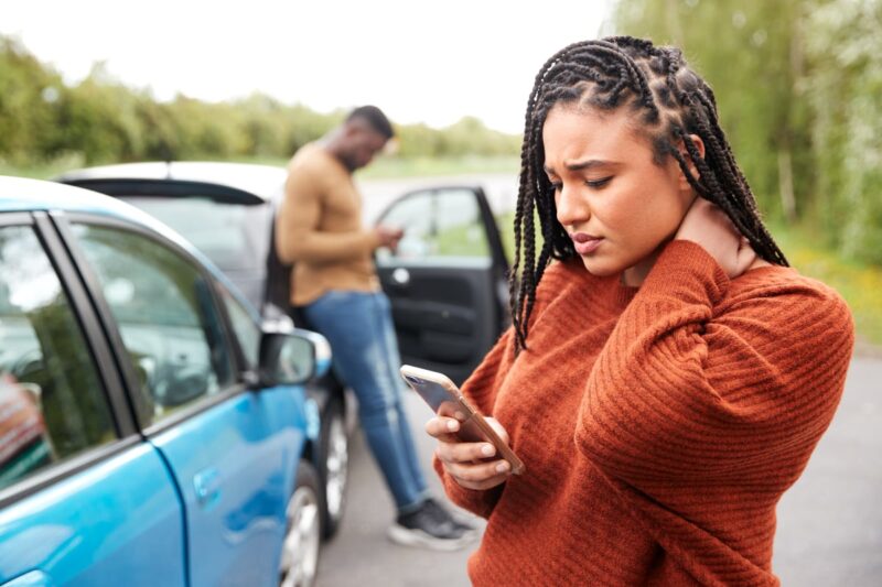 person holding neck and looking at phone after a car accident