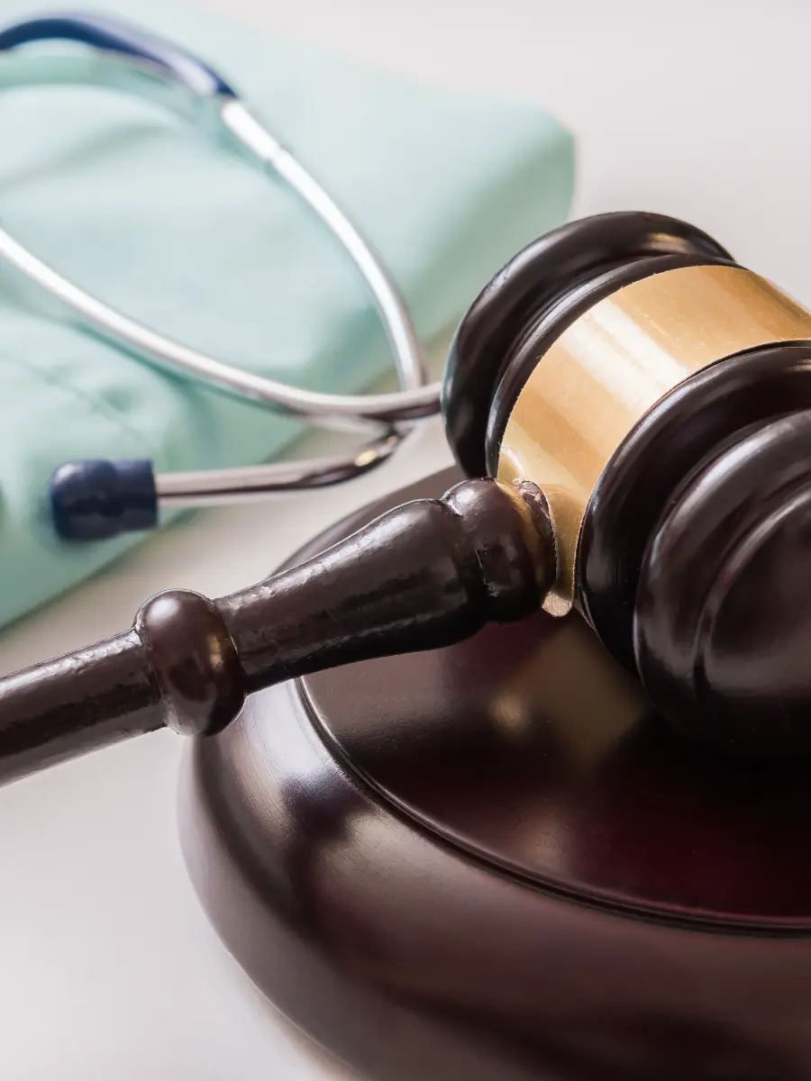 A judge's gavel lying next to a stethoscope on top of scrubs.