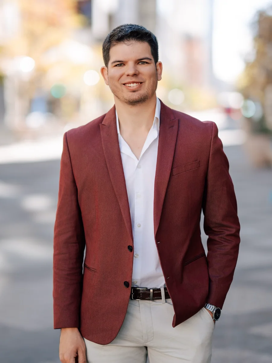 Attorney Josh Jacobson; a smiling young man wearing a blazer and slacks in front of a blurred street view.