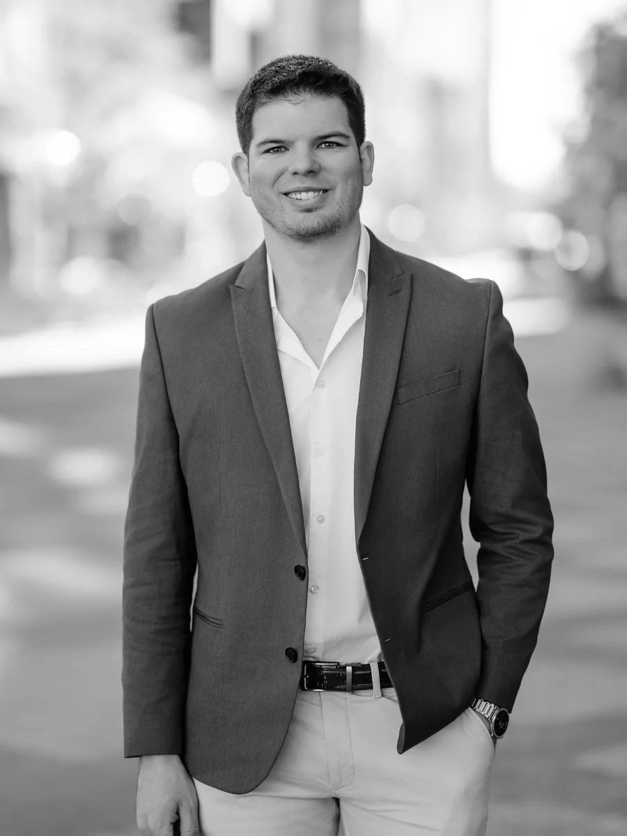 Attorney Josh Jacobson; a smiling young man wearing a blazer and slacks in front of a blurred street view.