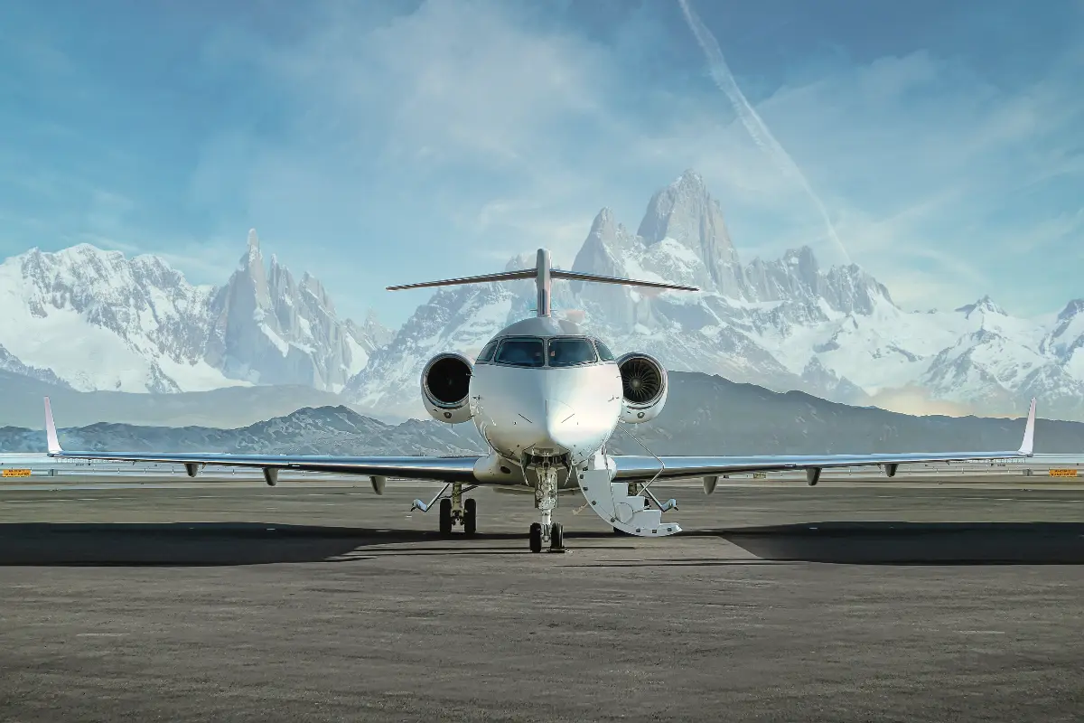 A sleek private jet is parked on a runway with its entrance stairs deployed, set against dramatic, snow-covered mountain peaks.